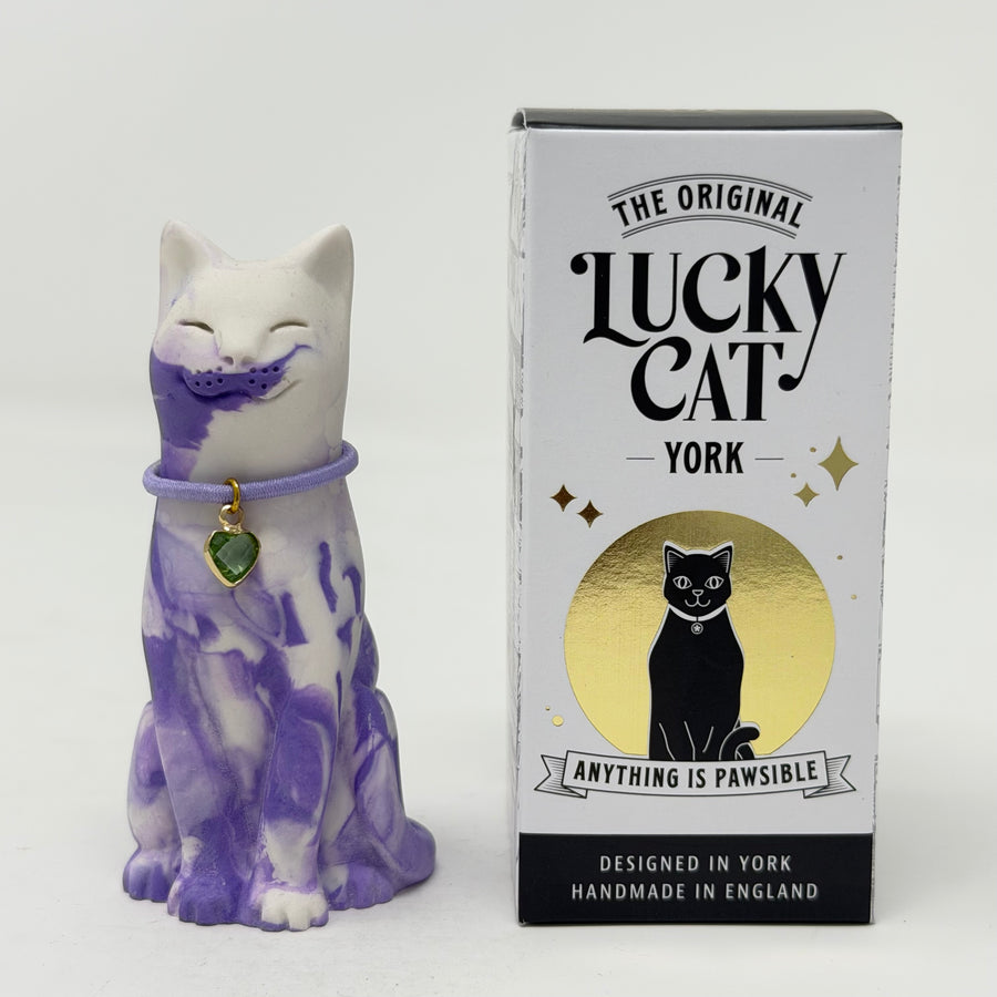 A lavender and white and marbled cat figurine wearing a purple collar with a green heart charm, shown next to its white packaging box labelled 'The Original Lucky Cat York'.