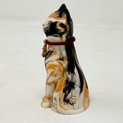 A marbled tortoiseshell Lucky Cat figurine wearing a burgundy collar with a gold letter B charm charm. Side view.