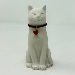 A white resin smiling Lucky Cat figurine wearing a burgundy collar with a red heart charm. Front view.