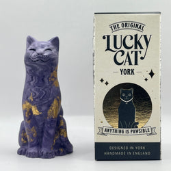 A purple lucky cat with with gold leaf accents stands beside branded box. The box reads 'The Original Lucky Cat York' and 'Anything Is Pawsible.