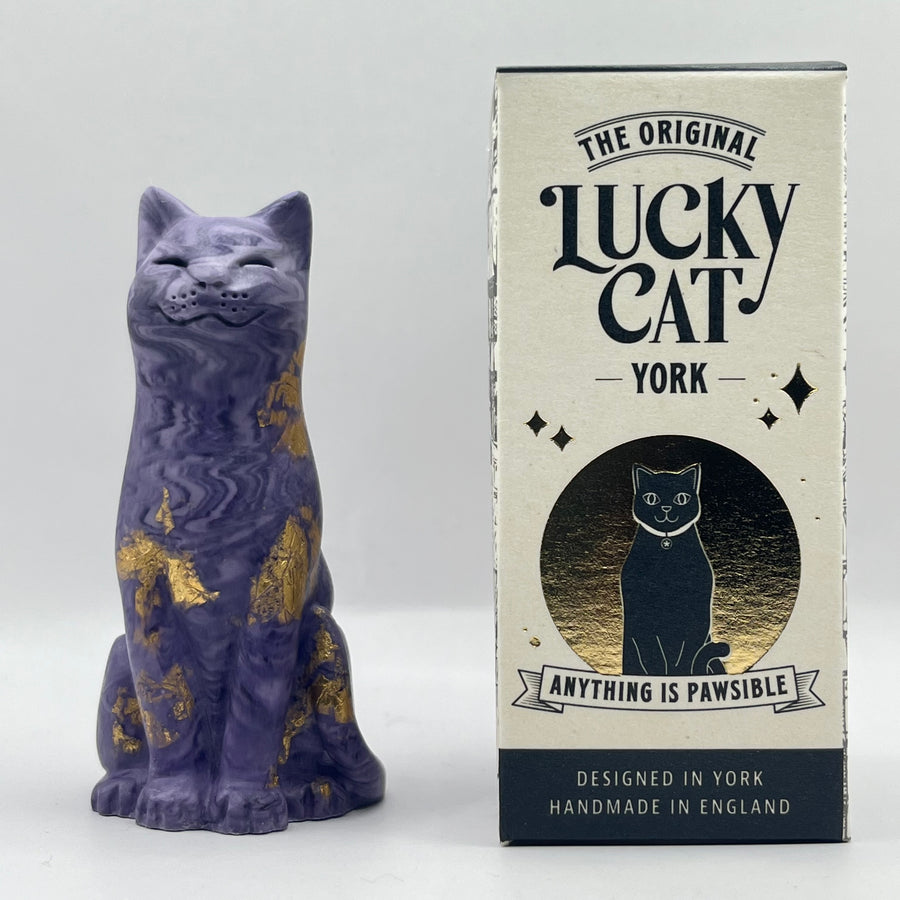 A purple lucky cat with with gold leaf accents stands beside branded box. The box reads 'The Original Lucky Cat York' and 'Anything Is Pawsible.