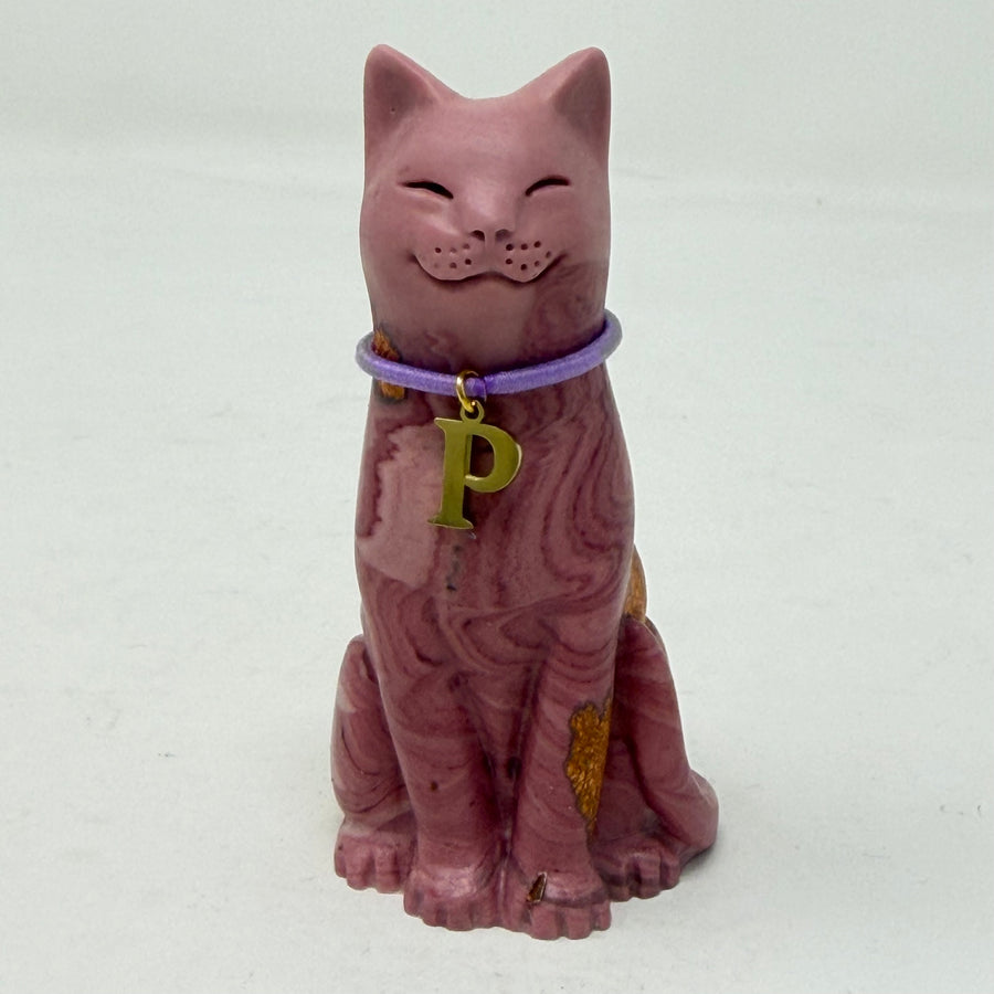 A marbled aubergine-coloured lucky cat figurine wearing a purple collar with a gold letter 'P' charm, set against a plain light grey background. Front view.