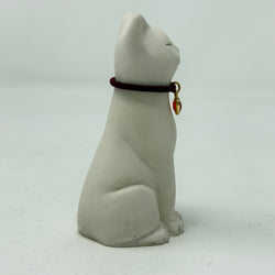 A white resin Lucky Cat figurine wearing a burgundy collar with a red heart charm. Side view.