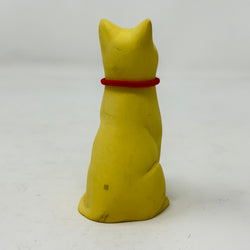 A smiling yellow lucky cat figurine wearing a red collar with a round Union Jack charm, photographed against a plain light grey background - rear view