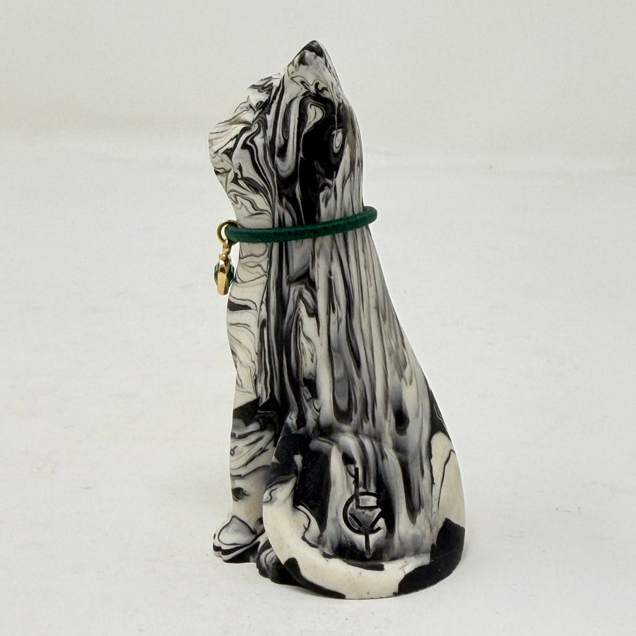 A marbled black and white Lucky Cat figurine wearing a green collar with a green heart charm. Side view.