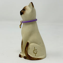 A  Lucky Cat figure hand painted to look like a chocolate point Siamese with a purple collar and heart pendant. Side view.