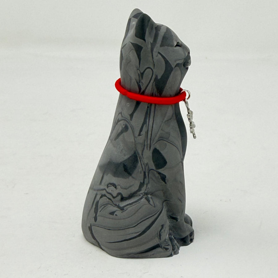 A grey marbled Lucky Cat figurine wearing a red collar with snowflake medallion charm. Side view.
