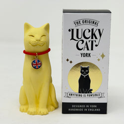 A yellow lucky cat figurine wearing a red collar with a Union Jack medallion, displayed next to its white and black retail box labelled 'The Original Lucky Cat York'.
