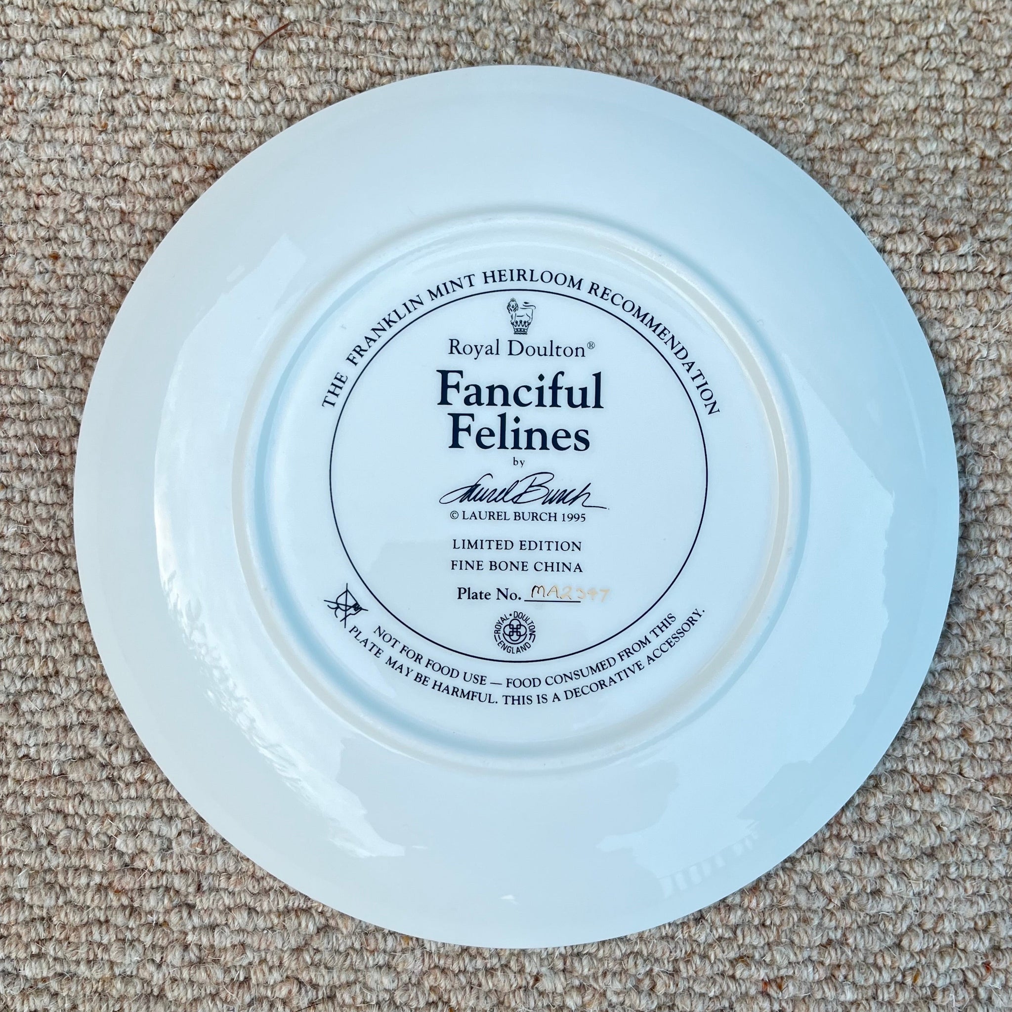 White plate with 'Fanciful Felines' branding on a beige carpet