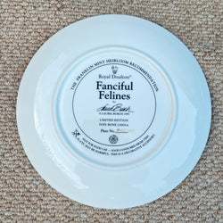 White plate with 'Fanciful Felines' branding on a beige carpet