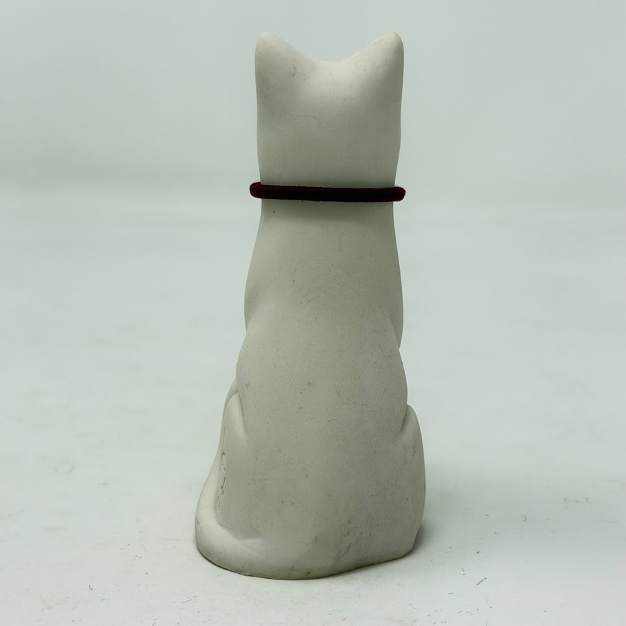 A white resin Lucky Cat figurine wearing a burgundy collar with a red heart charm. Rear view.