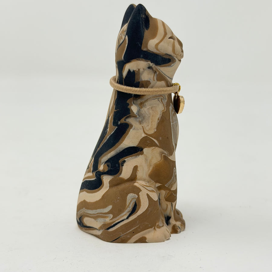A marbled cream brown and black tabby Lucky Cat figurine wearing a brown collar with a red heart charm. Side view.