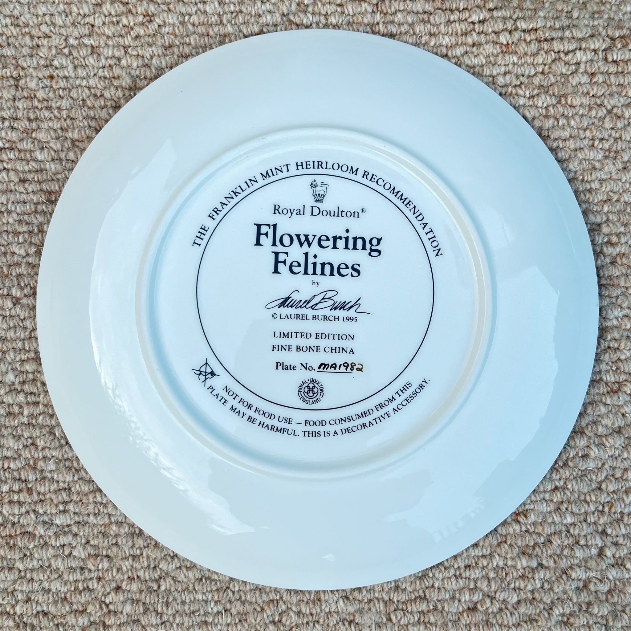 Decorative plate with 'Flowering Felines' text on a beige carpet