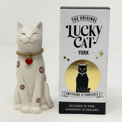 A white resin Lucky Cat figurine with red and white Yorkshire Rose decoration and a red heart charm, standing next to its white, black, and gold Original Lucky Cat  retail packaging box.