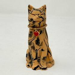 A resin cat figurine with a tan and black marbled pattern, wearing a brown collar with a red heart-shaped charm, set against a plain white background. Front view.