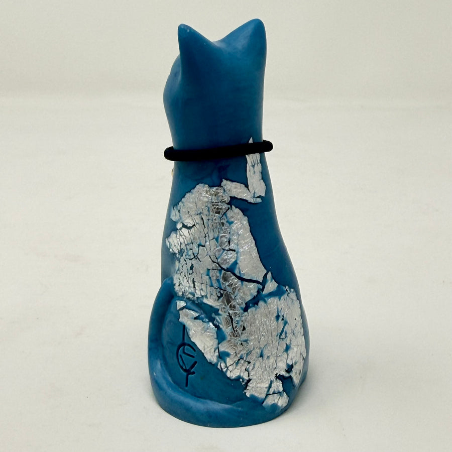 A blue lucky cat figurine with silver foiled details and a black collar with blue heart charm on a light grey background - rear view