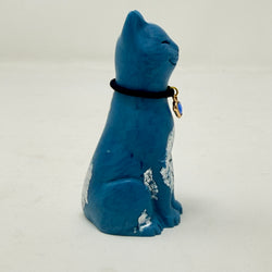 A blue lucky cat figurine with silver foiled details and a black collar with blue heart charm on a light grey background - side view