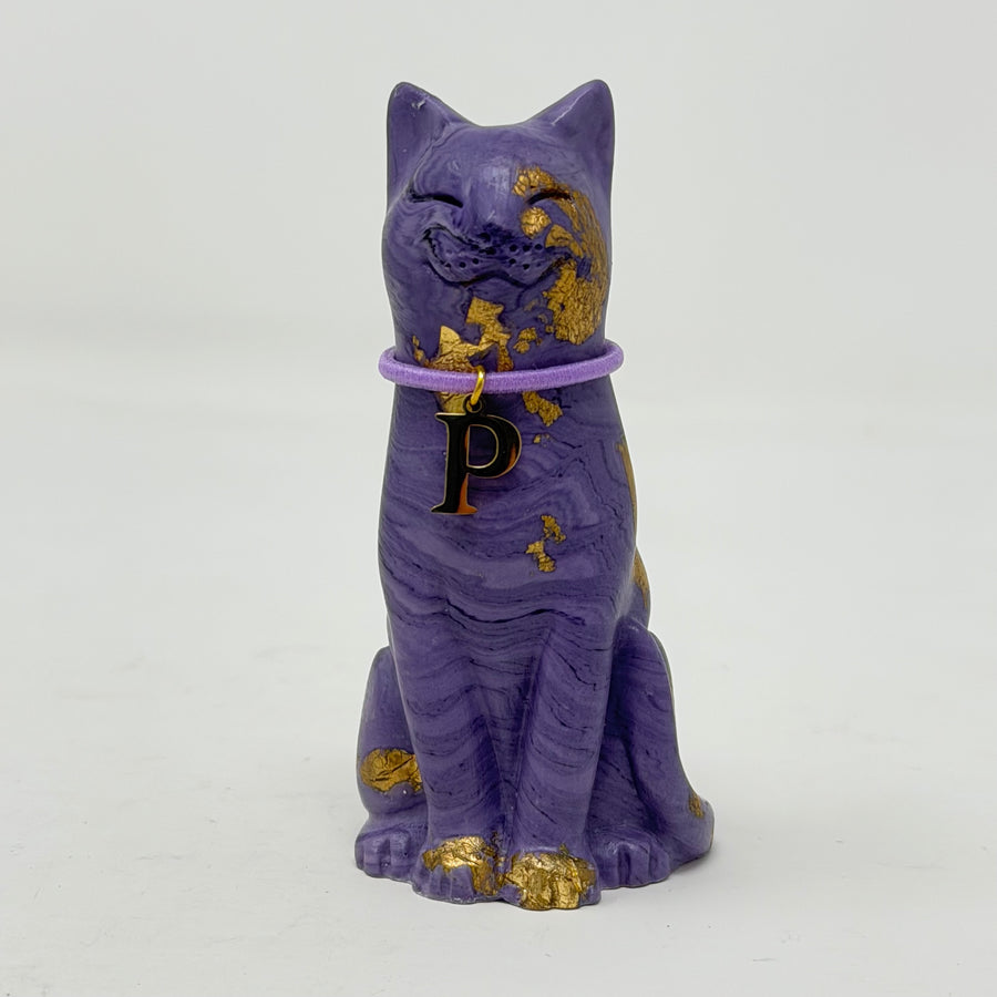 A purple lucky cat ornament with gold foil accents and lilac collar with P charm 