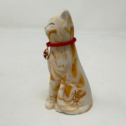 A ginger and white marbled Lucky Cat figurine wearing a red collar with a Union Jack medallion charm. Side view.