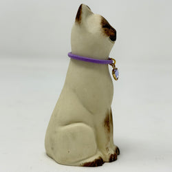 A  Lucky Cat figure hand painted to look like a chocolate point Siamese with a purple collar and heart pendant. Side view.