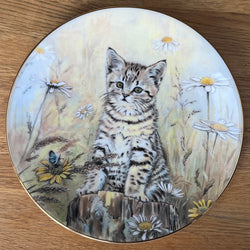 Decorative plate with a painting of a kitten and flowers on a wooden surface