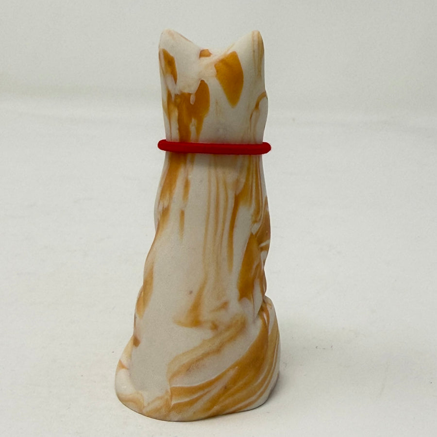 A ginger and white marbled Lucky Cat figurine wearing a red collar with a Union Jack medallion charm. Rear view.