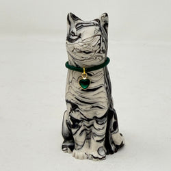 A marbled black and white Lucky Cat figurine wearing a green collar with a green heart charm. Front view.