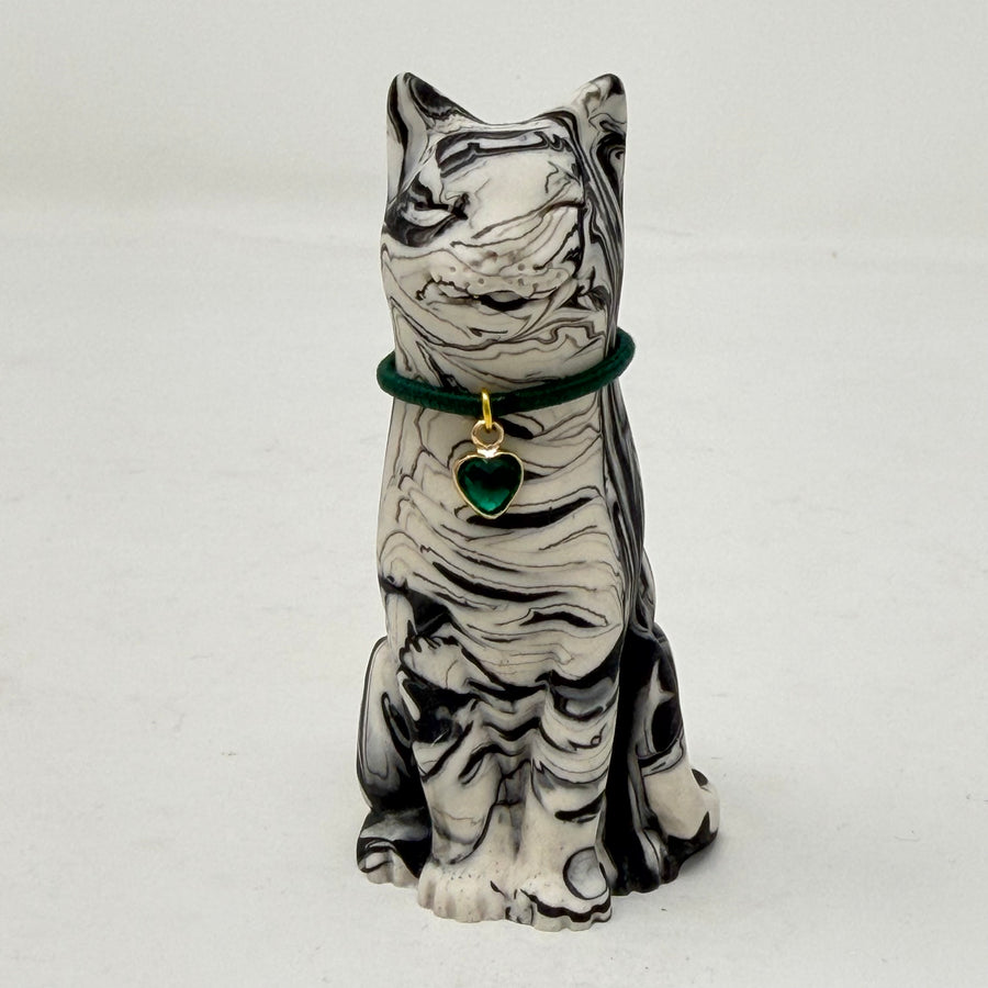 A marbled black and white Lucky Cat figurine wearing a green collar with a green heart charm. Front view.