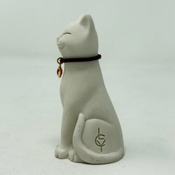 A white resin Lucky Cat figurine wearing a burgundy collar with a red heart charm. Side view.