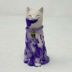 A lavender and white and marbled cat figurine wearing a purple collar with a green heart charm. Front view.