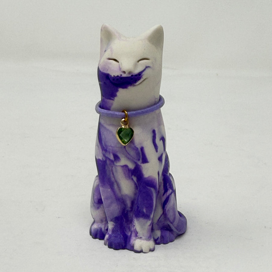 A lavender and white and marbled cat figurine wearing a purple collar with a green heart charm. Front view.