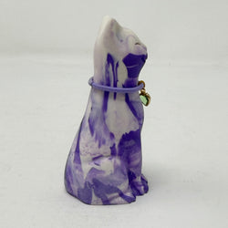 A lavender and white and marbled cat figurine wearing a purple collar with a green heart charm. Side view.
