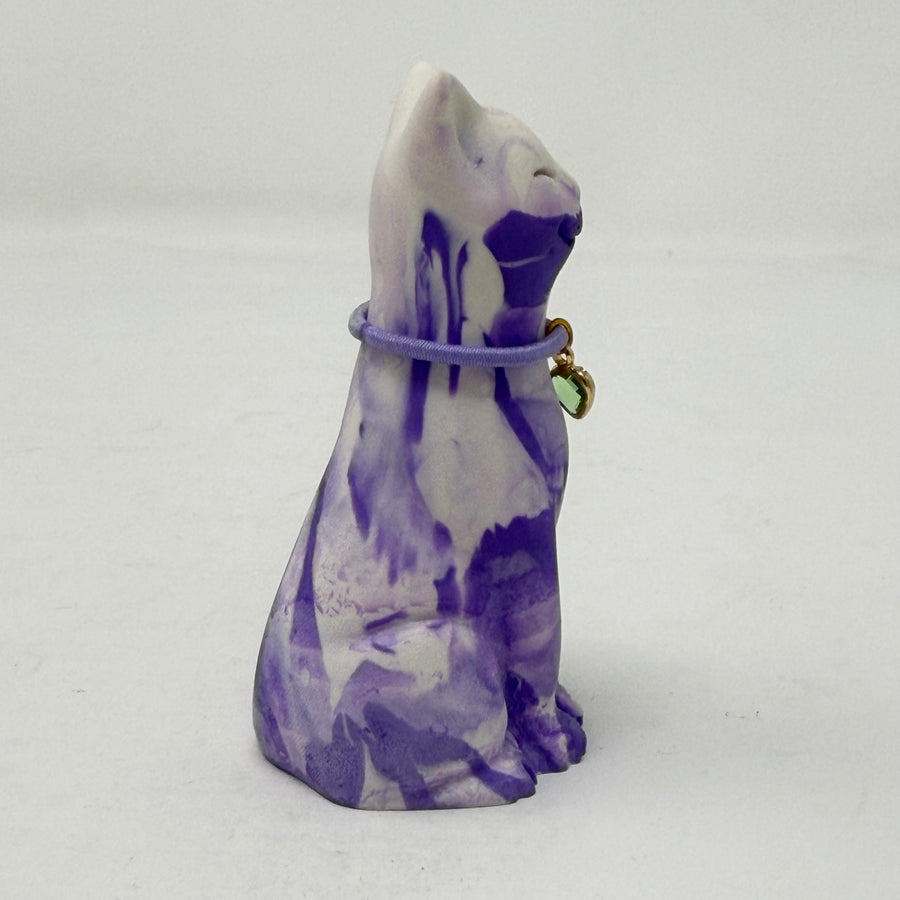 A lavender and white and marbled cat figurine wearing a purple collar with a green heart charm. Side view.
