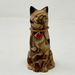 A marbled cream brown and black tabby Lucky Cat figurine wearing a brown collar with a red heart charm. Front view.