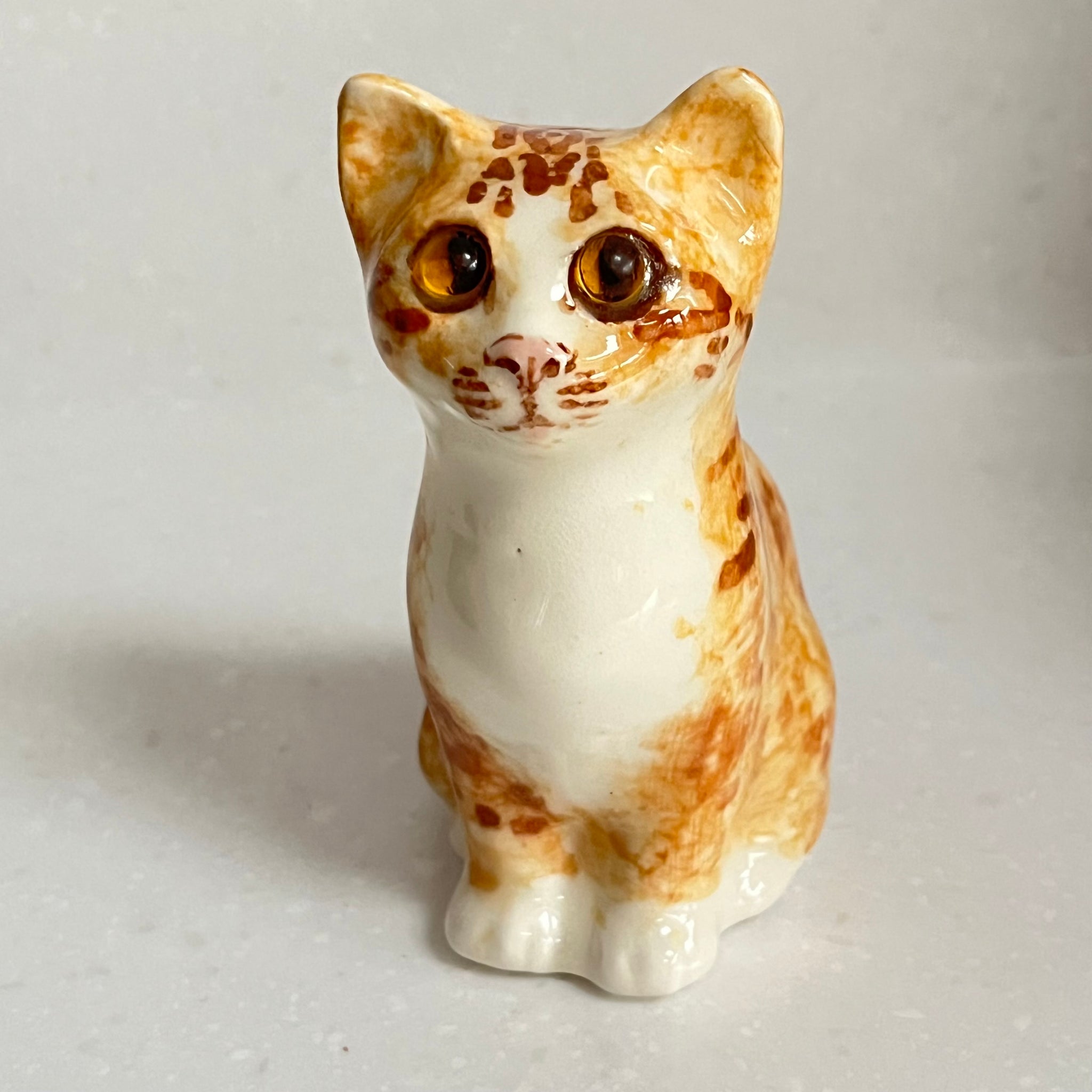 Small ceramic cat figurine with brown and white pattern on a light gray background