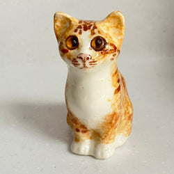 Small ceramic cat figurine with brown and white pattern on a light gray background