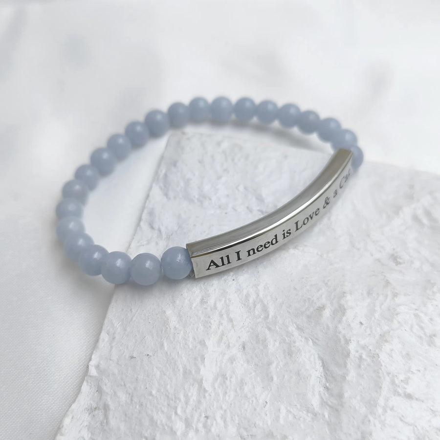A light blue beaded bracelet with a polished silver bar engraved with the words 'All I need is Love & a Cat