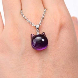 A hand holding a purple cat head shaped pendant on a silver coloured chain