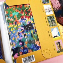 A close-up of a colourful notecard wallet, showing a black cat illustration over a vivid floral field on the cover