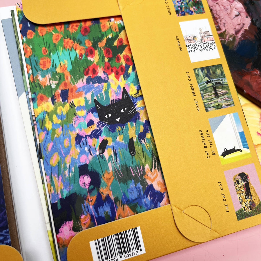 A close-up of a colourful notecard wallet, showing a black cat illustration over a vivid floral field on the cover