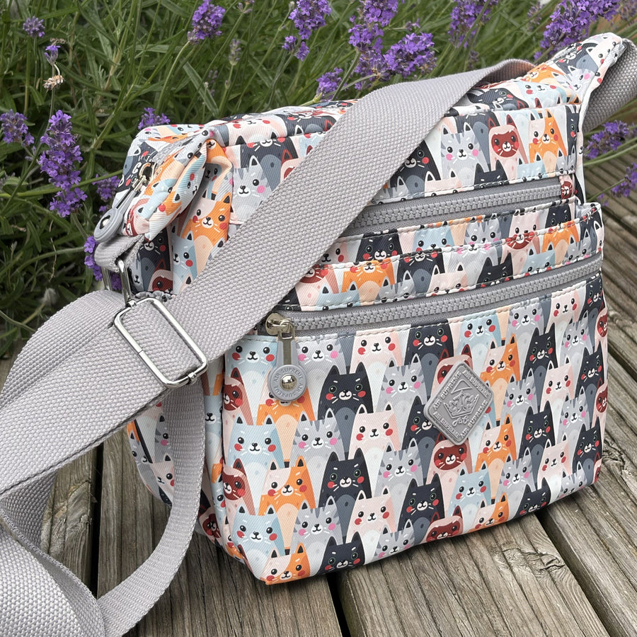 Multicolored cat-patterned bag with a grey strap on a wooden surface with lavender in the background