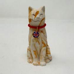A ginger and white marbled Lucky Cat figurine wearing a red collar with a Union Jack medallion charm. Front view.