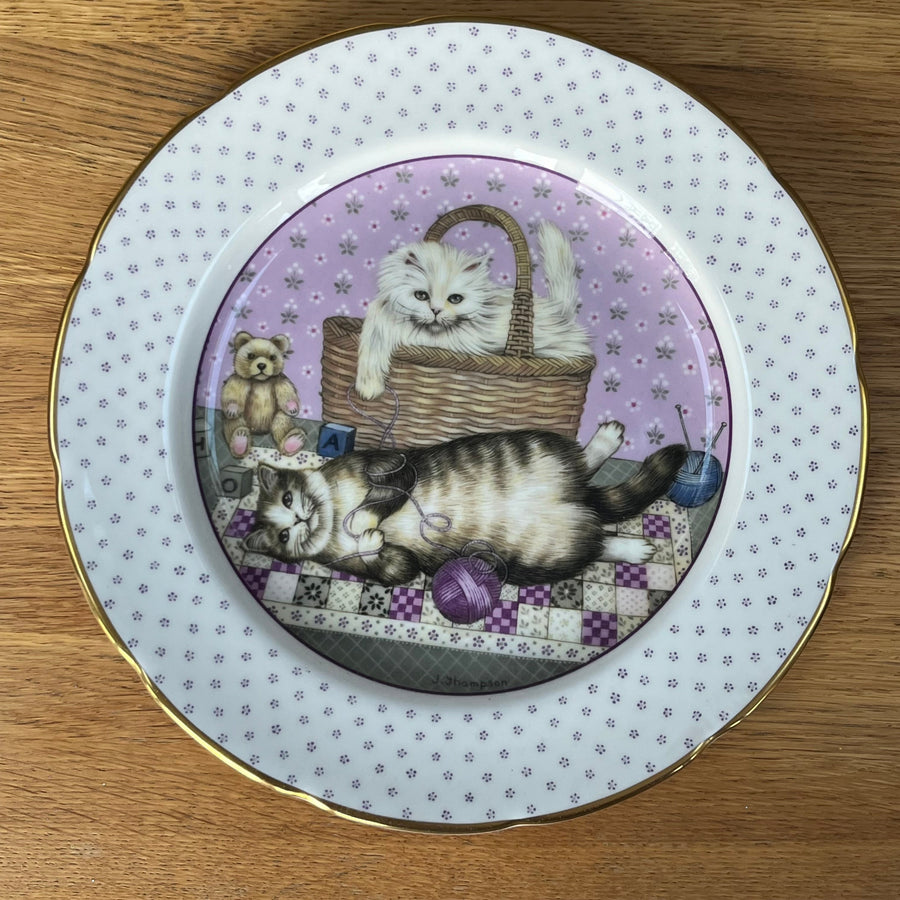 Decorative plate with a design of two cats  on a purple background, placed on a wooden surface.