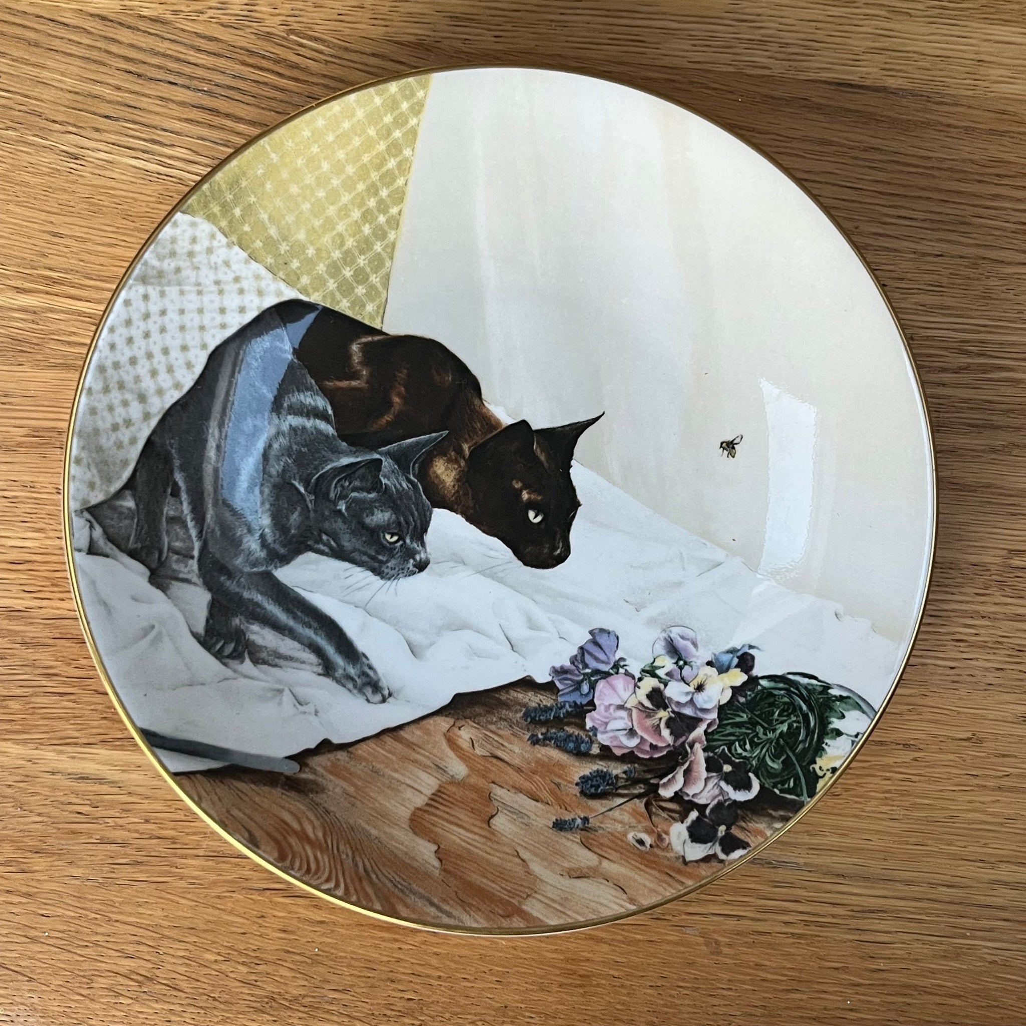 Decorative plate with artistic depiction of cats and flowers on a wooden surface