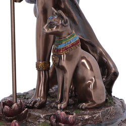 Bronze statue of a cat with colorful collar and staff on a white background