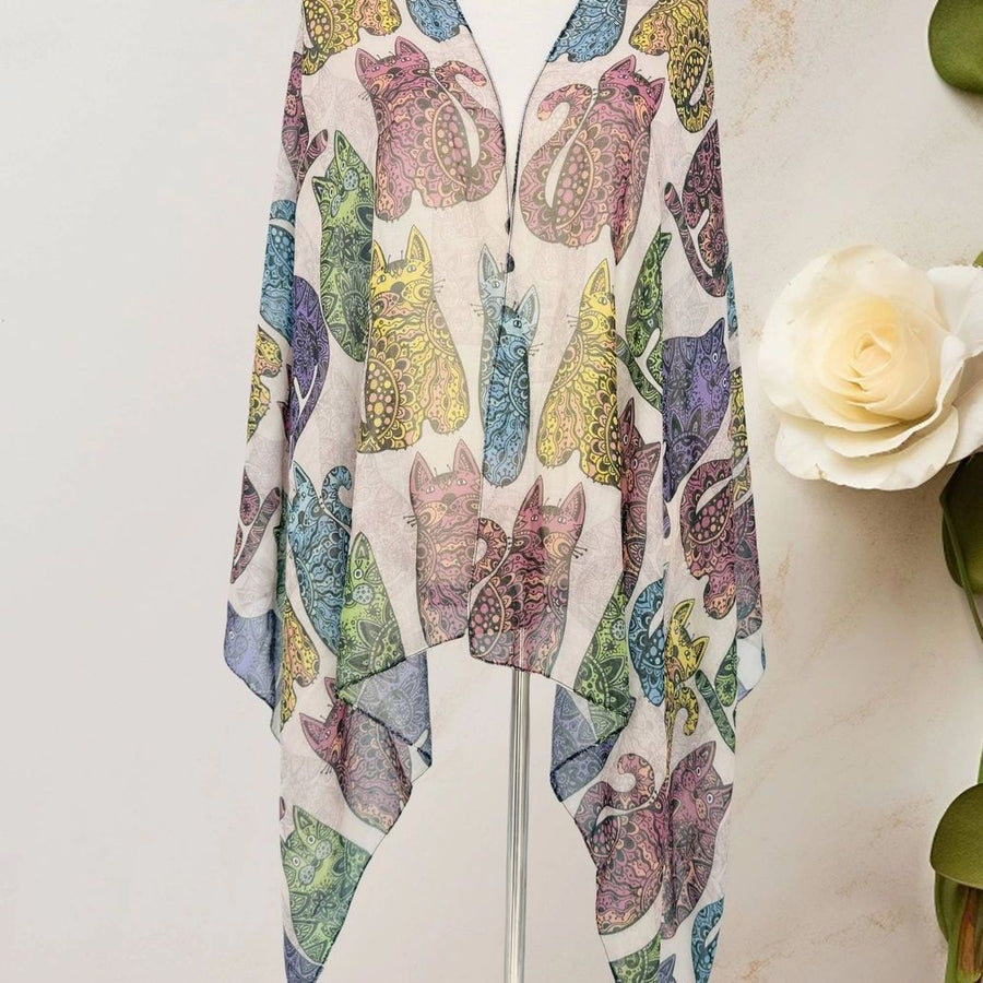 A lightweight scarf or kimono-style wrap displayed on a mannequin stand, featuring a colourful print of stylised cats in muted purple, blue, green, and yellow tones