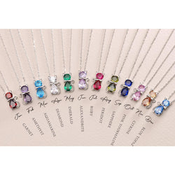 A collection of cat-shaped birthstone pendants on silver chains, each pendant is a different colour representing various birth months