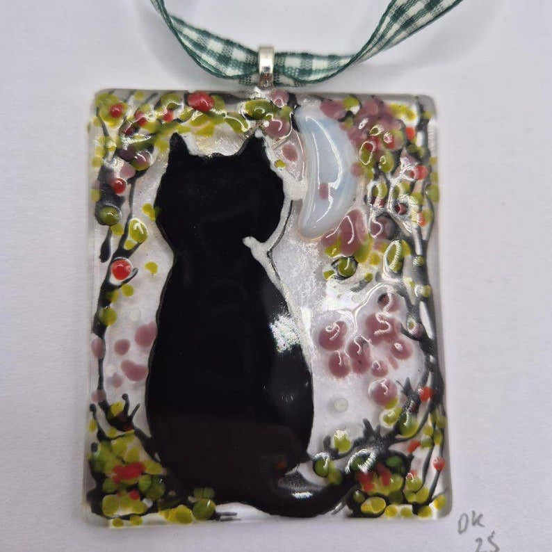 A square glass pendant ornament featuring a black cat silhouette against a white and pink floral background, suspended from gingham ribbon
