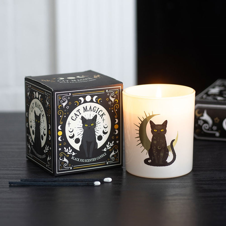 Candle with a black cat design next to its packaging on a dark surface.