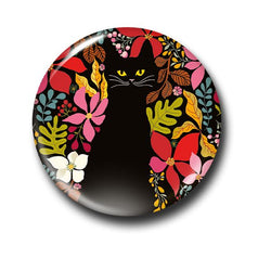 A round magnet badge featuring a black cat surrounded by colourful tropical flowers on a black background